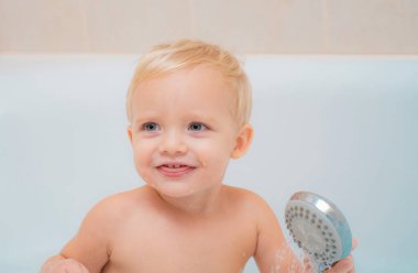 Komik şirin bebek banyo köpüğü içinde yüzüyor. Tatlı küçük bebek çocuk alarak banyo beyaz bir güneşli banyo köpük ve ördek oyuncaklar ile oynama