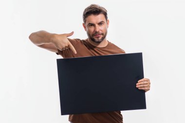 Boş afişi olan adam, stüdyo arka planında izole edilmiş. Elinde boş boş afiş tutan, işaret eden ve işaret parmağı taşıyan bir adam var. Erkek pano ya da afiş sunar