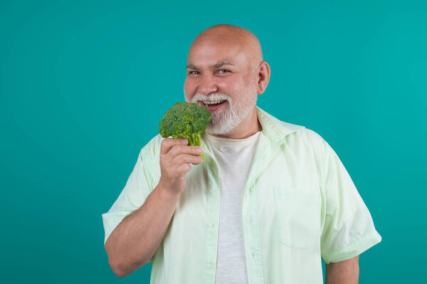 Счастливого старшеклассника. Сильный старик держит брокколи. Мускулистый старший на диете изолирован в студии. Веганский выпускник. Зрелый на диете. Стареющая диета. Сильный выпускник. Диета для пожилых людей