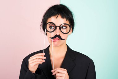 Siyah peruklu genç bir kadın sahte bıyığı pozitif ve mutlu yapıyor. Komik kız gülüşü. Genç transseksüel kadın. Komik kadın suratı. Çekici, suratını buruşturan komik kızın portresi. Duygu Kadını