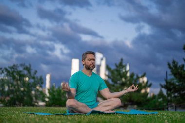 Sport Man dışarıda çimenlerde nilüferde meditasyon yapıyor. Sporcu şehir parkında yoga yaparken asana meditasyonu yapıyor. Atletik erkek meditasyonu, rahatlama, sağlıklı yaşam tarzı kavramı. Açık havada meditasyon.