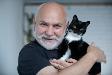 Yaşlı büyükbaba tüylü kedisine sarılıyor. Emekli adam ve kedisi evde. Yaşlı adam kedisine sevgiyle bakıyor. Son sınıf öğrencisi ve kedileri evde. Yaşlı büyükbaba ve tüylü kedisi