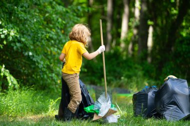 Çocuk parkı temizliyor, çöpü çöp torbasına koyuyor. Çevresel koruma. Çocuk temizlik için çöp poşeti topluyor. Çöpler için siyah torbada çöp bulundurmak. Kirlilik ve geri dönüşüm