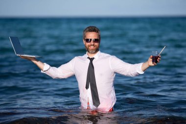 Fun business lifestyle. Freelance work, distance online work, e-working. Summer business. Business man in shirt remote working on laptop in sea water. Business man working online clipart