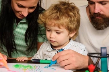 Ebeveynler ve küçük çocuklar birlikte oynuyorlar. Neşeli oğul, anne ve babasıyla resim çiziyor ve eğleniyor. Çocuk resim öğrenme, küçük ressam resmi, çizim