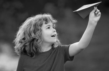 Küçük çocuk kağıt uçak tutuyor. Oyuncak uçak çocukların elinde. Mutlu çocuk eğiliyor ve sarı kağıt uçak fırlatıyor. Çocuk kağıt uçakla oynuyor. Kağıt uçakla oynayan çocuk