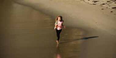 Okyanus boyunca koşan küçük bir çocuk. Çocuk kumsalda koşuyor. Koşmak ve çocuklar için sağlıklı spor