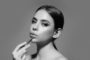 Studio portrait of beautiful woman with red lipstick. Beautiful young woman applying lipstick on her lips, isolated on studio background