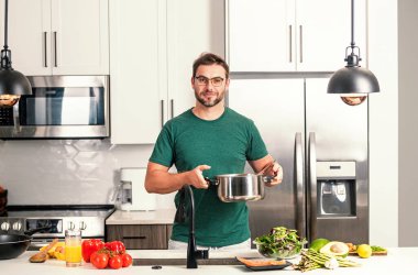 Aşçı adam mutfakta tencerede yemek pişiriyor. Gurme yemeği hazırlama süreci. Adam evde yemek pişiriyor, esrar kullanıyor. Şef yemek pişiriyor. Yakışıklı aşçı aşçı konsepti