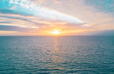 Gün batımında gökyüzü ve bulutların arasında güneş olan sakin bir deniz. Okyanus ve gökyüzü arkaplanı, deniz manzarası