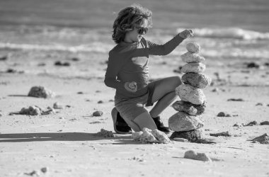 Deniz sahilinde zen taşları olan çocuk, meditasyon, spa ve uyum. Sakin denge kavramı. Çocuklar sahilde oynar. Sakin olun. Sakinleştirici çocuk ve denize karşı taş kule. Plajda meditasyon için Zen Taşları