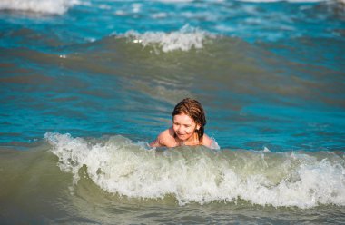 Mutlu çocuk yaz plajında hayatın tadını çıkarıyor. Güneşli bir günde denizde dalgaların arasında küçük bir çocuk. Arka planda okyanus ya da deniz dalgaları