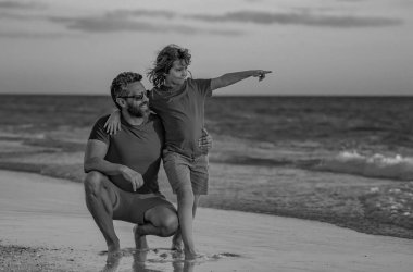 Baba ve oğul sahilde birlikte yürüyorlar. Babalık aile kavramı. Babanızla denize açılın. Kumsalda, yaşam tarzında ve yaz tatilinde rahatla. Baba ve çocuk yaz denizinde yürür. Fayher Günü