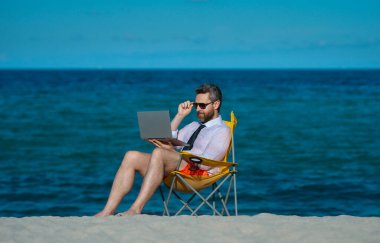 Çılgın özgür iş adamı. Eğlenceli iş hayatı. Deniz sahilinde dizüstü bilgisayarı olan yakışıklı bir iş adamı. Komik iş adamı. Serbest konsept, yaz işi. İş başarısı