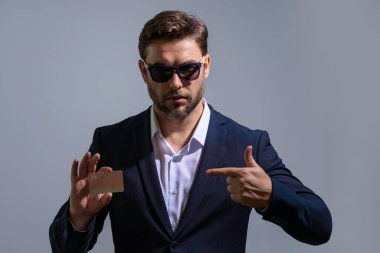 Gri arka planda plastik kredi kartı gösteren bir iş adamı portresi. İş ve başarı kavramı. İnternetten alışveriş. Çevrimiçi ödeme. Kredi kartının bakiyesi
