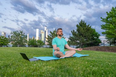 Sport Man dışarıda çimenlerde nilüferde meditasyon yapıyor. Sporcu şehir parkında yoga yaparken asana meditasyonu yapıyor. Atletik erkek meditasyonu, rahatlama, sağlıklı yaşam tarzı kavramı. Açık havada meditasyon.