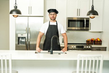Üniformalı yakışıklı aşçı mutfakta yemek yapıyor. Restoran menüsü konsepti. Fırıncı üniformalı İspanyol adam. Aşçılık ve aşçılık. İş üniformalı, siyah önlüklü, şef şapkalı bir aşçı.
