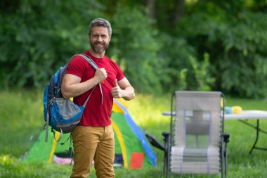 Turistler doğada kamp yapmayı seviyor. Doğaya yaz gezisi. Orman kampında dinlenen adam. Kamp gezisi. Yürüyüşten sonra çadırın yanında dinleniyor. Barışçıl bir kamp alanında özgürlük tatili. Yazın piknikteki adam