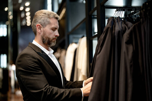 Мужчина носит классический костюм, когда делает покупки в бутике. Классический костюм для успешного бизнесмена. Модный магазин с костюмами. Зрелый человек выбирает костюм. Мужчина выбирает костюм для официального мероприятия