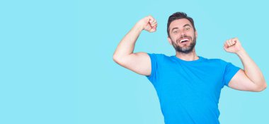 Kazanan. Başarılı bir adam kollarını kaldırdı. Kollarını kaldırıp başarıyı kutlayan heyecanlı adam. Mavi arka planda izole edilmiş heyecanlı bir erkek modelin portresi. Kutlama yapan adam kazanır. Başarı. Heyecanlı kazanan