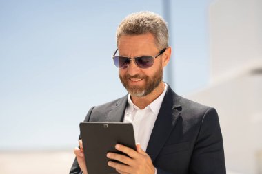 Açık havada tablet kullanan mutlu bir iş adamı. Tabletle başarılı bir iş adamı. Dışarıda tablet üzerinde çalışan bir iş adamı. Zarif iş adamı tableti kontrol ediyor. Dijital aygıt kullanan işadamı