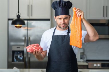 Bin yıllık İspanyol şef üniformalı adam mutfakta balık ve et, somon ve biftek tutuyor. Balık ve et pişiriyorum. Balık ve etli restoran menüsü. Yemek pişirme, balık ve et reklamı konsepti
