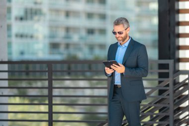Açık havada tabletle başarılı bir iş adamı. Kendine güvenen bir iş adamı dışarıda tablet kullanıyor. Olgun iş adamı girişimci finans verilerini kontrol eder. Zengin bankacı tabletteki sözleşmeyi gözden geçiriyor