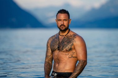 Seksi yaz erkeği. Suda ıslak kaslı erkek vücudu. Çıplak seksi erkek vücudu. İnsan yaz doğasında suya su sıçratır. Yaz plajında poz veren formda bir adam. Dağdaki gölde su sıçratan güçlü adam.