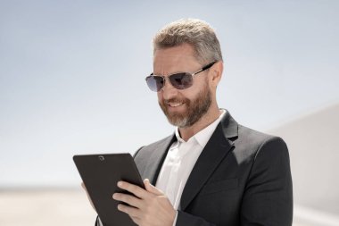 Açık havada tablet kullanan mutlu bir iş adamı. Tabletle başarılı bir iş adamı. Dışarıda tablet üzerinde çalışan bir iş adamı. Zarif iş adamı tableti kontrol ediyor. Dijital aygıt kullanan işadamı