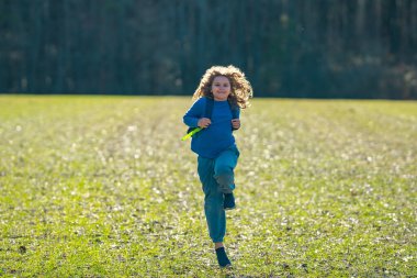 Çocuk sahada koşuyor. Dışarı koşan mutlu çocuk. Çocuk doğada zıplıyor ve koşuyor. Çocuk çayırda koşuyor. Aktif çocuklar için yaz eğlencesi. Neşeli çocuk özgürlüğü. Tasasız çocukluk.