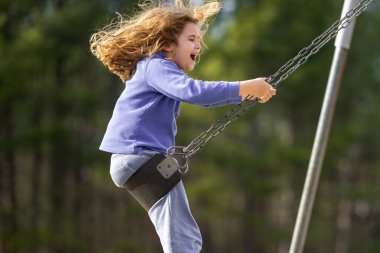 Heyecanlı çocuk eğleniyor. Çocuk bahçesinde mutlu bir çocuk. Havada sallanan tasasız çocuk. Mutlu çocuklar dışarıda oynuyor. Genç çocuk heyecanla sallanıyor. Dışarıdaki oyuncu çocuk. Komik çocuk yüzü.