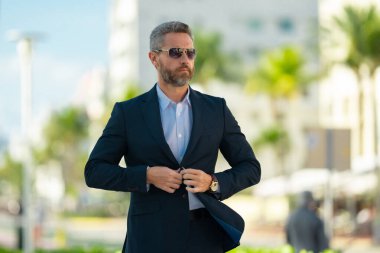 Olgun iş adamı şehirde güvenle yürüyor. Sokakta yürüyen bir iş adamı. Ofise doğru yürüyen yakışıklı bir iş adamı. Açık havada yürüyen kendinden emin bir girişimci.