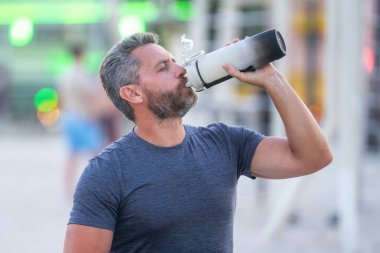 Spor salonundaki adam bir bankta dinleniyor ve su şişesinden su içiyor. Antrenmandan sonra bir bankta oturan olgun bir spor modeli. Fitness sonrası ara veren bir adam spor su şişesinden su içer.