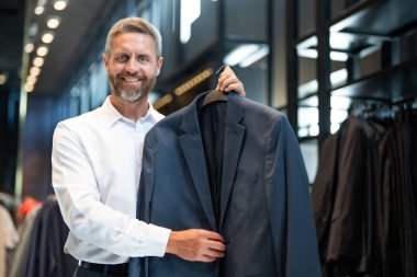 Bir adam butikte alışveriş yaparken klasik bir terzi kıyafeti giyer. Başarılı bir iş adamı için klasik bir kıyafet. Takım elbiseli modaya uygun bir mağaza. İş adamı takım elbise seçer. Bir erkek resmi etkinlik için takım elbise seçer.