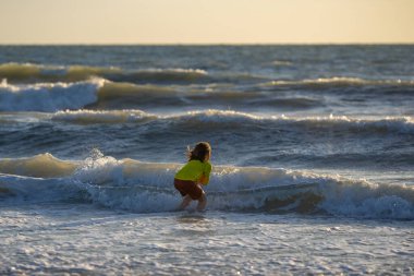 Çocuk yaz günü tropikal plajda koşuyor ve oynuyor. Çocuk açık hava aktivitelerinin tadını çıkarıyor. Denizde yaz tatili. Gün batımında sahilde koşan küçük bir çocuk. Yaz tatilindeki çocuklar