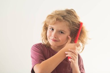 Beyaz stüdyo arka planında izole edilmiş saçlarını tarayan küçük bir çocuğun yakın plan portresi. Kıvırcık saçlı çocuk saç fırçası ya da tarak tutuyor. Sağlıklı saçlar. Çocuk kontrolsüz saçlarını tarıyor.