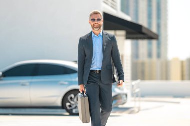 Başarılı bir iş adamı evrak çantasıyla dışarıda dolaşır. İş adamı evrak çantasını dışarıda tutuyor. Takım elbiseli olgun iş adamı. Şirket işi. Takım elbiseli zengin iş adamı. Açık hava iş portresi