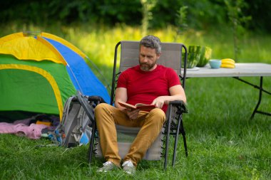 Adam doğada kamp yapmayı seviyor. Doğaya yaz gezisi. Orman kampında dinlenen bir turist. Kamp gezisi. Yürüyüşten sonra çadırın yanında dinleniyor. Barışçıl bir kamp alanında özgürlük tatili. Yazın piknikteki adam
