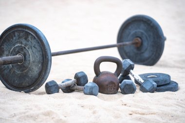Kettlebell ve ağırlık arka planı. Ağır ağırlıklarla vücut geliştirme. Dambıllarla park egzersizi. Ağırlıklarla spor sahnesi. Kettlebell, halterler ve halterler. Kumsalda ağırlık çalışması.