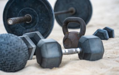 Salonda demir halterler var. Kum üzerinde spor aletleri. Açık havada güç kaldırma. Aktif yaşam tarzı egzersizi. Ağır kettlebell eğitimi. Açık spor salonu geçmişi. Metal dambıllar. Kentsel fitness. Doğal egzersiz.