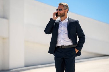 Ofis çalışanı dışarıda cep telefonuyla konuşuyor. Girişimci cep telefonundan konuşur. Yönetici telefon görüşmesi yapıyor. Telefon kullanan şık bir iş adamı. İş görüşmesi. Meşgul iş adamı telefonda konuşuyor.