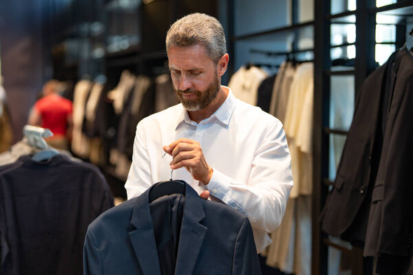 Мужчина носит классический костюм, когда делает покупки в бутике. Классический костюм для успешного бизнесмена. Модный магазин с костюмами. Деловой человек выбирает костюм. Мужчина выбирает костюм для официального мероприятия