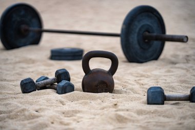 Kettlebell ve ağırlık arka planı. Ağır ağırlıklarla vücut geliştirme. Dambıllarla park egzersizi. Ağırlıklarla spor sahnesi. Kettlebell, halterler ve halterler. Kumsalda ağırlık çalışması.