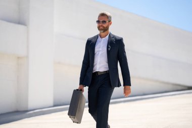 Açık hava iş portresi. Dışarıda yürüyen bir iş adamı. Şirket lideri harekete geçti. Çantalı takım elbiseli adam. İşadamı işe gidiyor. Evrak çantalı şehir işadamı. İşadamı ofise git.