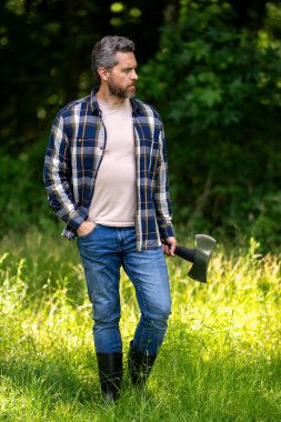 Olgun Oduncu 'nun ciddi suratı ormanda balta tutuyor. Baltalı bir oduncu kesmeden önce ağacı inceler. Ciddi bir oduncu. Millennial orta yaşlı adam elinde büyük bir balta tutuyor.