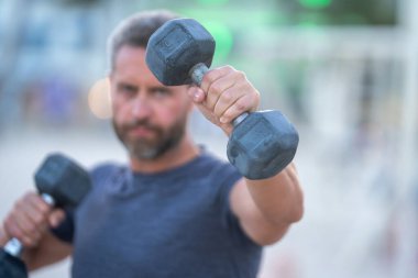 Dambıllar kol kola. Yetişkin bir adamın dambılları dışarı kaldırması. Kol kasları dambıl egzersizi yapıyor. Kol halteri tutun. Dambılı bir erkek kolunun yakın çekimi.