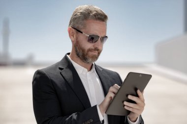 Dışarıda tablet kullanan bir iş adamı. Tabletli başarılı bir iş adamı. Şirket lideri iş adamı tablet üzerinde çalışıyor. Zarif iş adamı tableti kontrol ediyor. İş adamı belgeleri inceliyor
