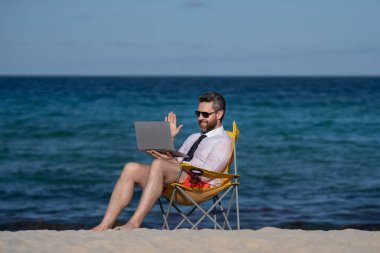 Deniz sahilinde dizüstü bilgisayar kullanan iş adamı. Yaz tatilindeki çılgın iş adamı. Heyecanlı iş adamı, çılgın komedi dünyası konsepti. Uzaktan kumanda çalışıyor. Yaz iş hayalleri