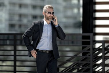 İş adamı telefonda konuşuyor ve yürüyor. Kendine güvenen bir iş adamı telefonla dışarı çıkar. İş telefonu konuşması. Şirket lideri telefonda konuşmakla meşgul. Zengin iş adamı. İş çağrısı