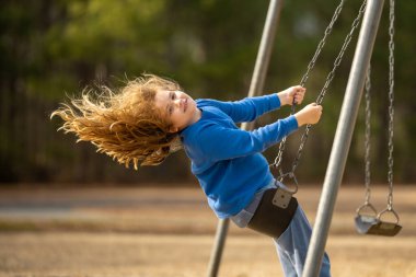 Bahar parkında sallanan neşeli çocuk. Sarı saçlı küçük bir çocuk salıncakta sallanıyor. Parkta gülümseyen mutlu çocuk. Mutlu çocukluk anları. Çocuk dışarıda oynuyor. Çocuk salıncakta eğleniyor. Çocuklar için açık hava oyunu